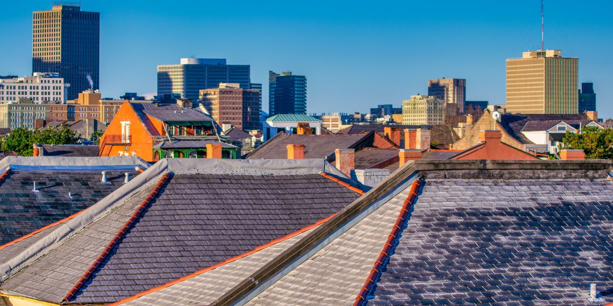 Rooftop view of historic buildings in the French Quarter with modern high-rise buildings in the background under a clear blue sky in New Orleans, Louisiana.
