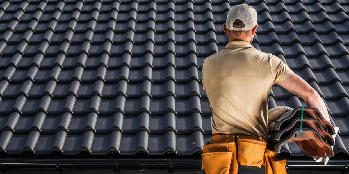 A professional roofer in work gear inspects a roof with neatly installed tiles, holding spare shingles. Showcases the expertise and precision of Priority Roofing's repair services.