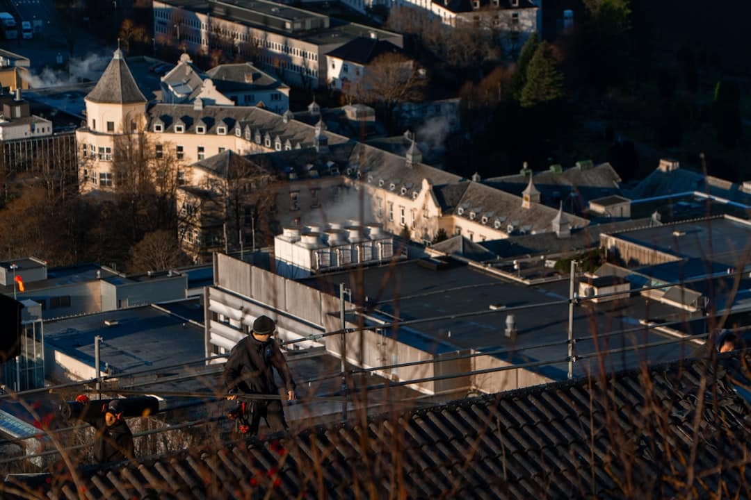 A professional roofer in safety gear carefully installing new shingles on a residential roof on a bright, sunny day, representing a trustworthy local contractor.