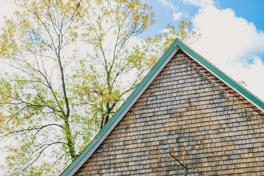 A professional roofer in safety gear meticulously installs new shingles on a residential roof on a bright, sunny day, showcasing expertise and quality craftsmanship.