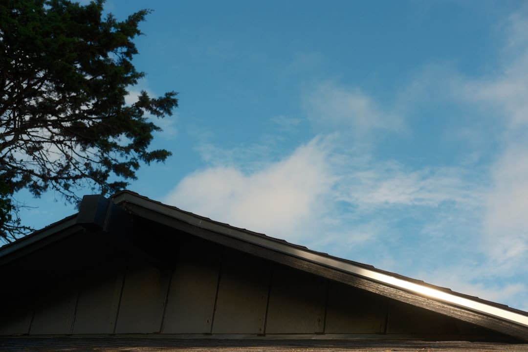 A damaged residential roof is covered by a bright blue tarp as a temporary repair, with dark, ominous storm clouds in the sky, representing vulnerability after a hurricane.