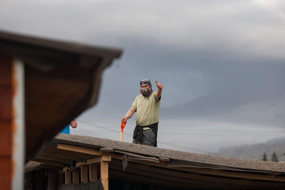 A professional roofing contractor carefully examining damaged shingles on a residential roof, representing a thorough post-storm inspection.