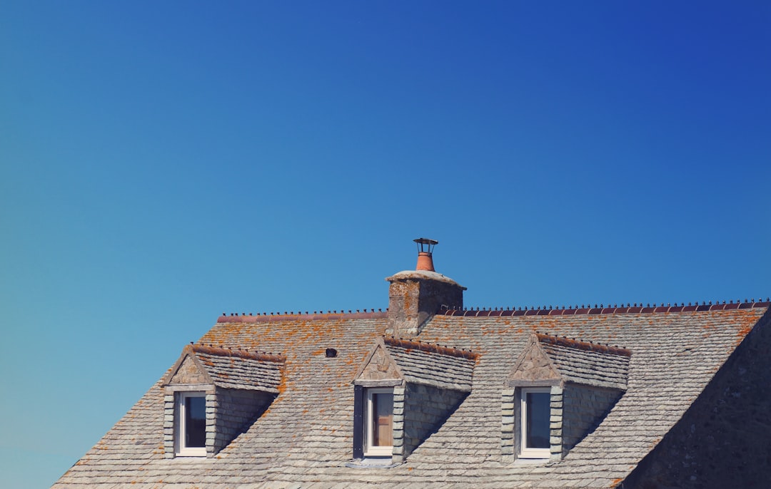 A professional roofing contractor stands on a ladder, looking at a residential roof to assess potential hurricane damage before beginning repairs.