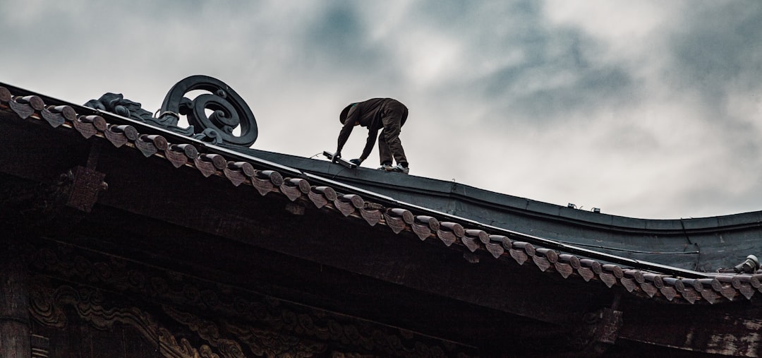 A roofer in professional gear carefully examining cracked and missing shingles on a house roof, conducting a post-storm inspection.