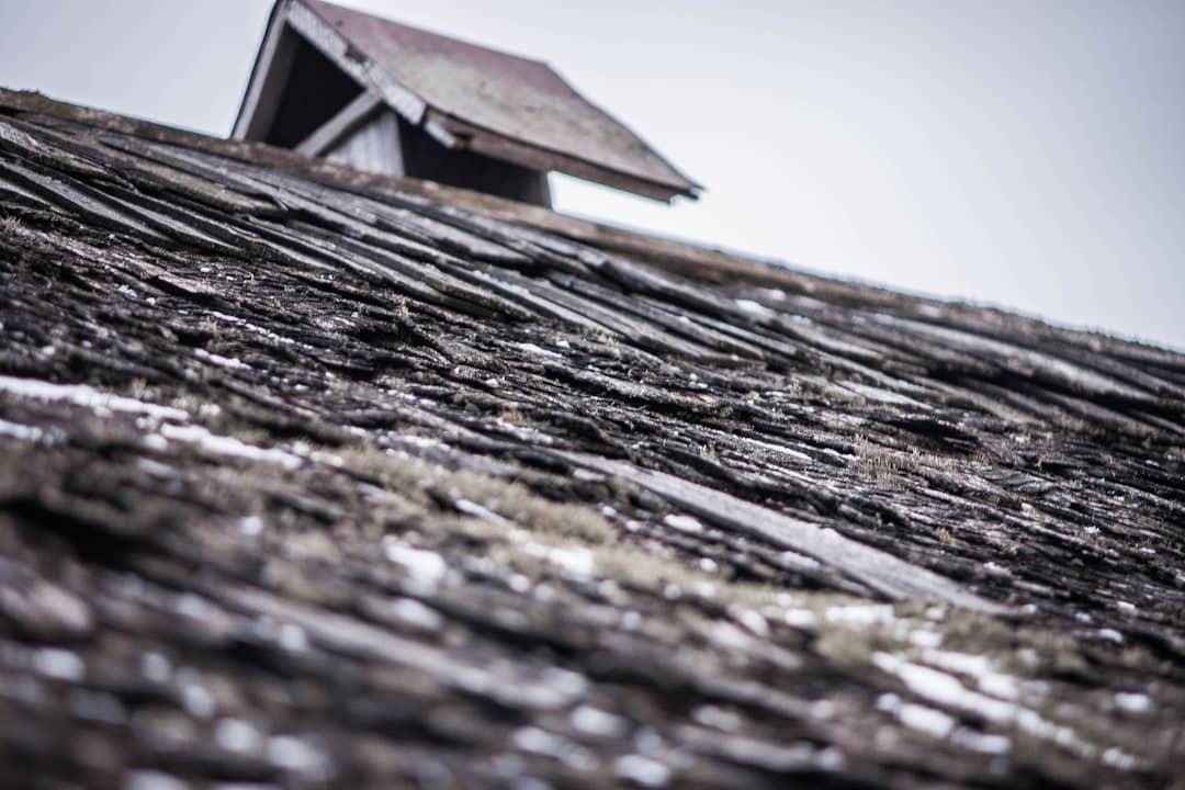 Close-up of a residential roof with many shingles torn off and damaged after a severe weather event, highlighting the failure of substandard roofing materials in the Gulf South.