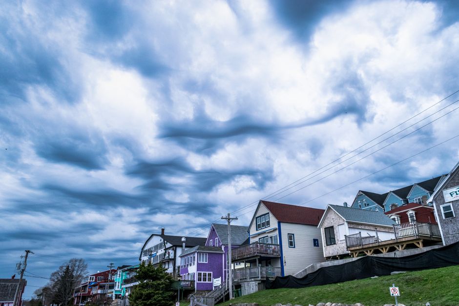 Dramatic, dark storm clouds gathering over a residential neighborhood, emphasizing the need for a durable roof to protect the home below.