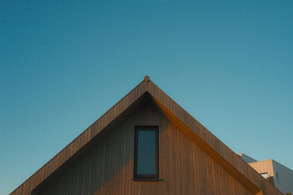 Professional roofing contractor in safety gear carefully inspects the shingles on a residential roof on a bright, sunny da...