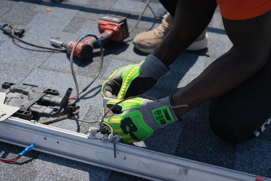 A skilled roofer in professional gear carefully installing new shingles on a residential roof, with the sun highlighting the quality of the work.