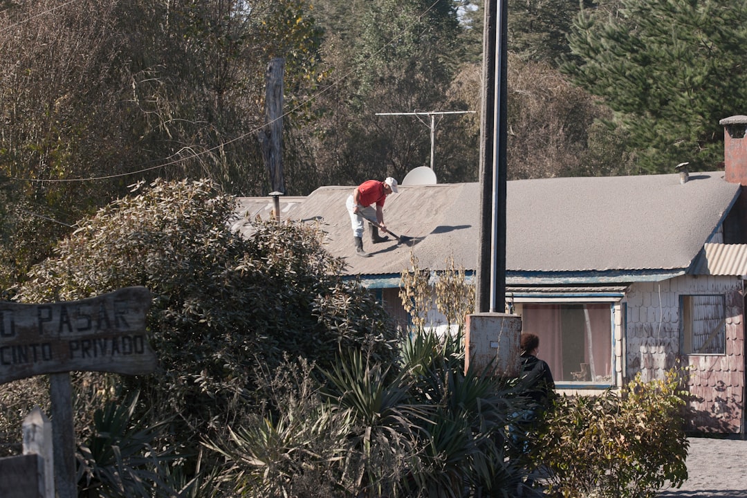 A skilled roofer in safety gear carefully installing new, high-quality shingles on a house under a clear blue sky, symbolizing the value and security of professional roof installation.