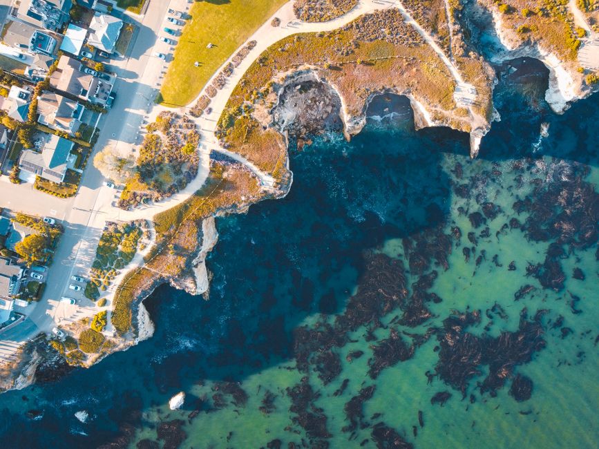 Aerial photograph of a large, multi-unit residential community with uniform roofs, situated near the sunny coastline, illu...