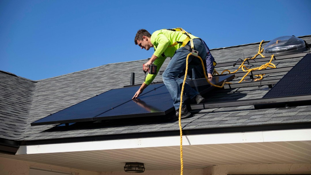 A professional and friendly local roofer carefully inspecting a residential roof on a bright, sunny day, representing trust and quality workmanship.