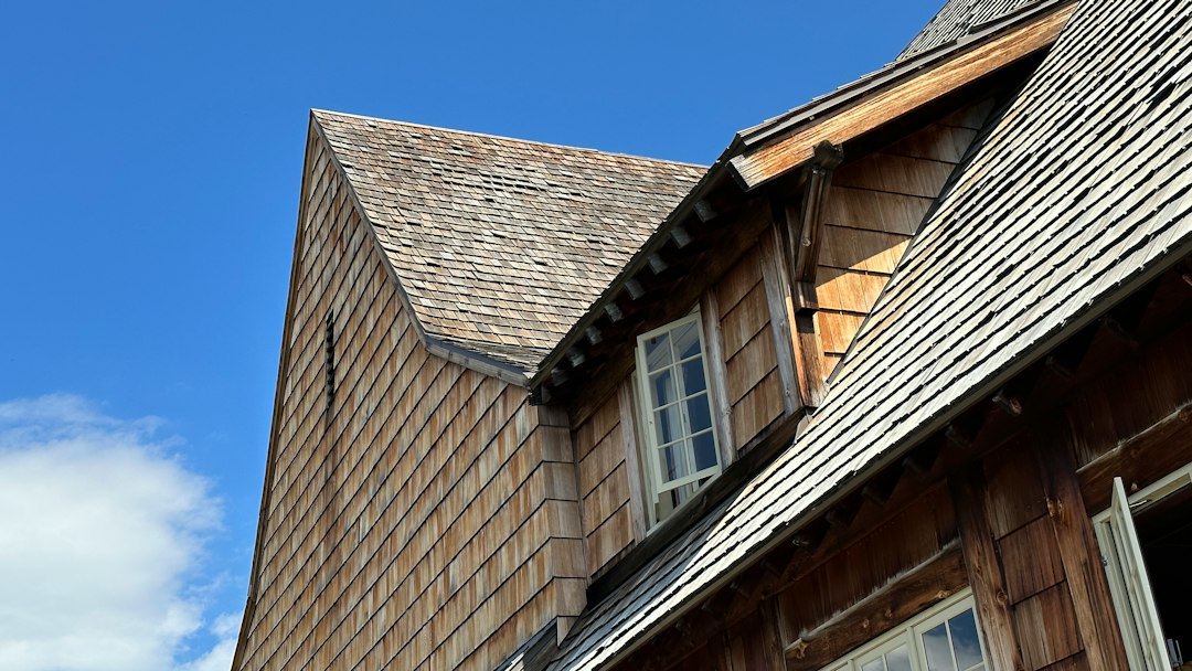 A skilled and professional roofer in clean gear carefully installs new shingles on a residential roof under a clear, sunny sky, representing quality and trust.