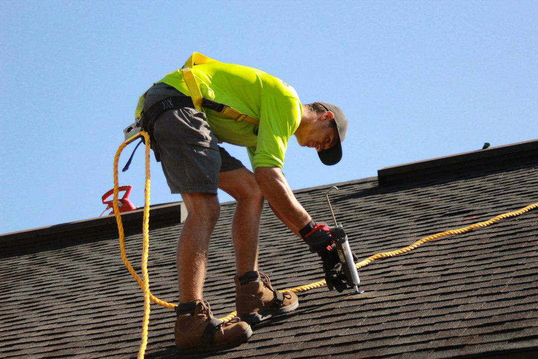 A skilled roofer in safety gear carefully fastens a shingle onto a new roof, representing expert installation and superior protection.