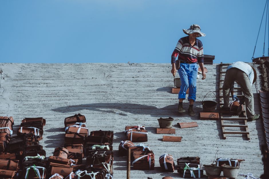 A skilled roofer in safety gear professionally installing new, corrosion-resistant shingles on a house with the coast visible in the background.