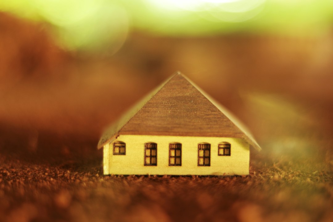 A small model of a house sits on a neat stack of coins against a clean background, symbolizing insurance savings and a smart financial investment.