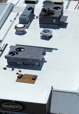 Completed commercial flat roof installation with HVAC units and white TPO membrane at a Church’s Texas Chicken restaurant, viewed from above.