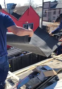Priority Roofing crew applying underlayment during roof repair over Pot Belly NOLA restaurant, with visible tools and materials on site.
